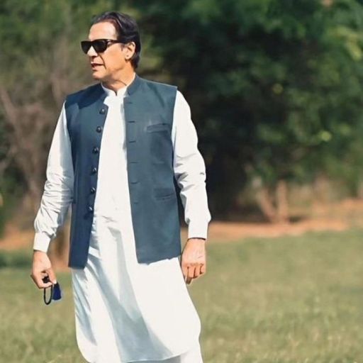 Person in traditional white attire with a dark waistcoat walking on grass