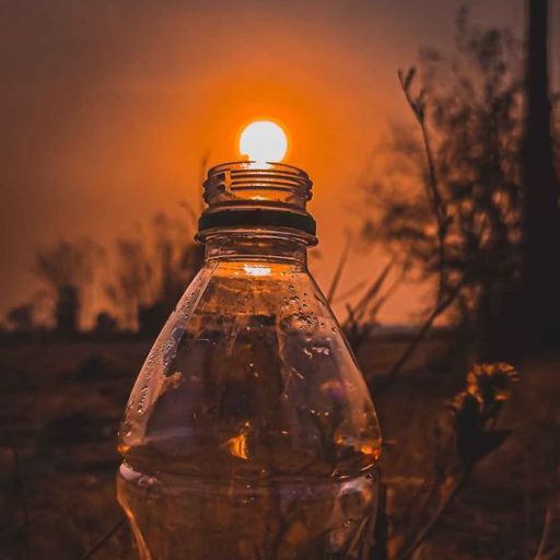 Sunset aligned with a bottle's opening, creating the illusion of a glowing bulb, with a warm-toned backdrop