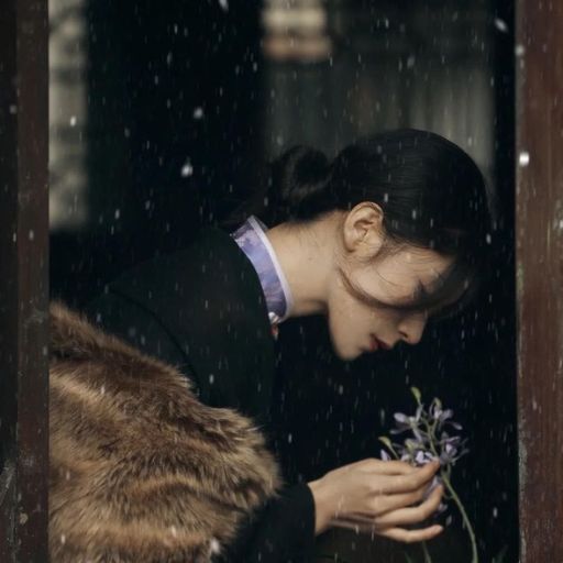 Woman in vintage attire holding flowers, leaning on a wooden door as snow falls