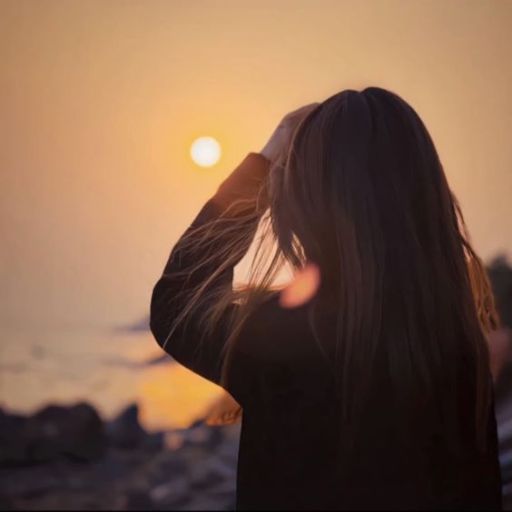 Woman watching sunset on beach, hand in hair, sun near horizon