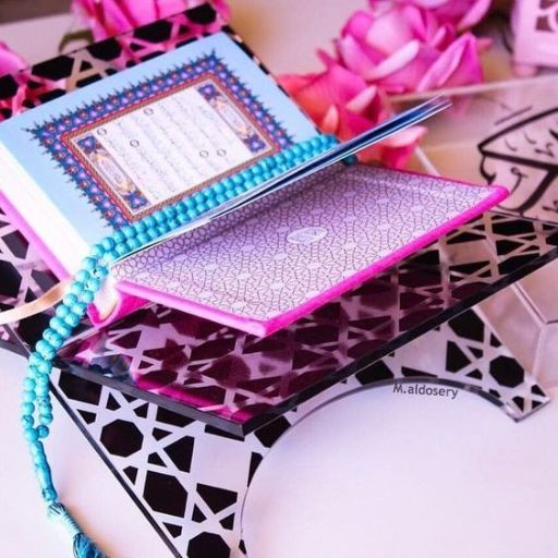 A Quran open on a stand with a blue beaded bookmark and pink petals around it