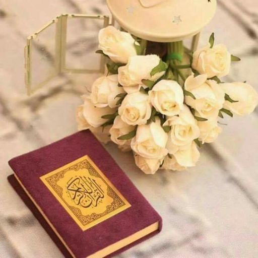 A book with Arabic script on its cover beside a bouquet of white roses and a mirrored box on a textured surface