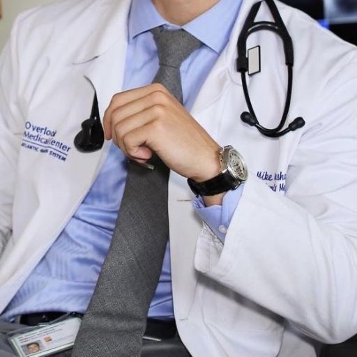 A cropped photo of a person in a doctor's coat adjusting a tie, with a stethoscope around their neck