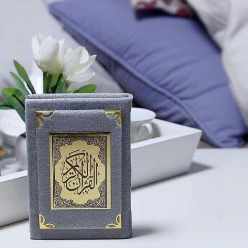 A gray book with Arabic script on the cover, placed on a table near a white flower and a blurred background