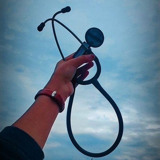 A hand holding up a stethoscope against a cloudy sky