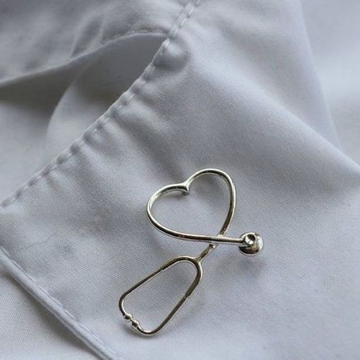 A heart-shaped silver pin on a white fabric surface