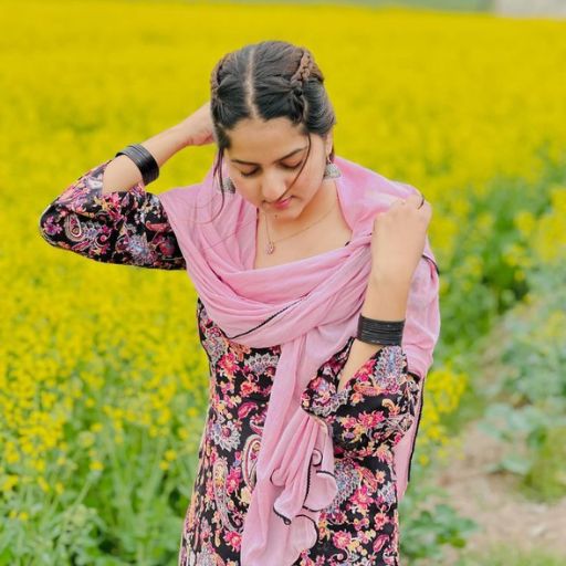 A person in a floral dress with a pink scarf standing in a yellow flowering field