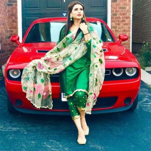 A person in green traditional attire standing in front of a red car