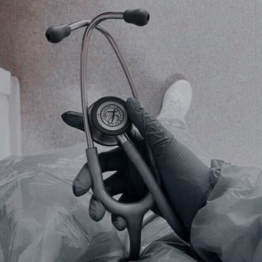 A person in medical gloves holding a stethoscope, with feet in the background on a hospital bed