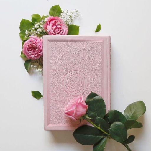 A pink book with an embossed cover beside fresh roses on a white background