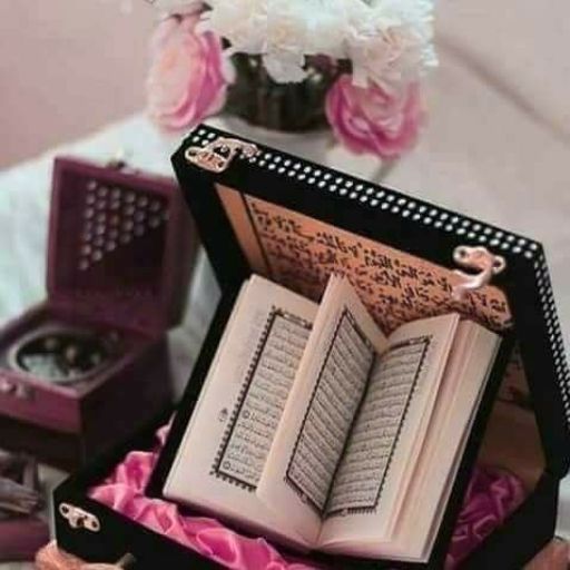 An open book in a decorative box beside a vase with flowers and another ornate box on a pink surface