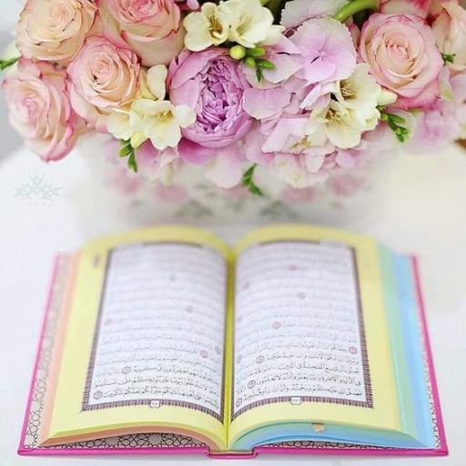 An open book with Arabic text in front of a bouquet of pink roses and purple flowers