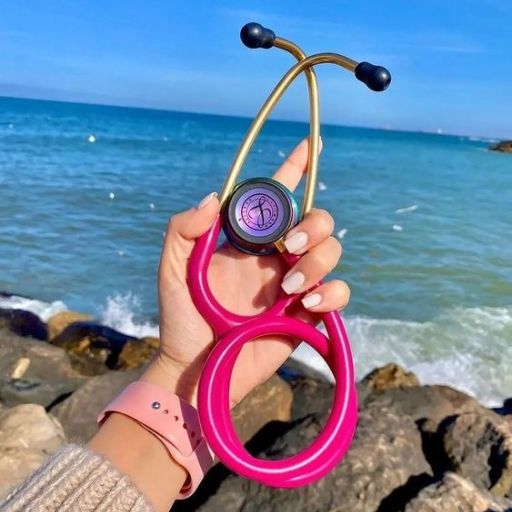 Hand holding a pink stethoscope with the sea and sky in the background