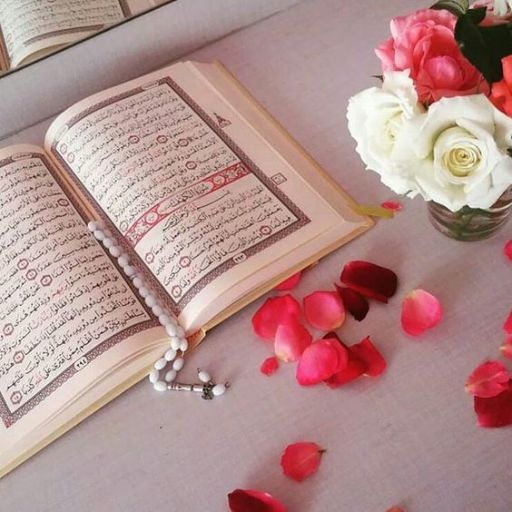 Open book with Arabic script, prayer beads, and a vase of roses on a table scattered with rose petals