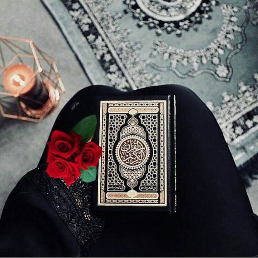 Person holding a book with intricate cover and roses on a patterned rug, candle in background