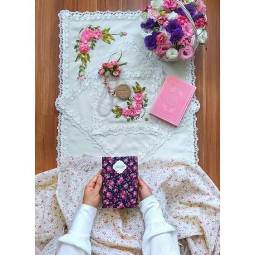 Person holding a floral book with a lace tablecloth, bouquet, cookies, and another book nearby