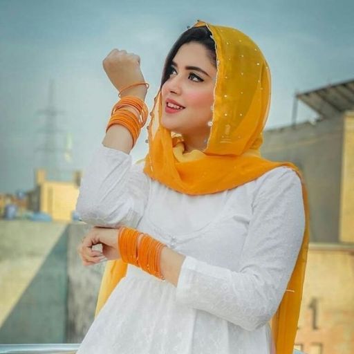 Person in white dress with yellow scarf and orange bangles, standing outdoors