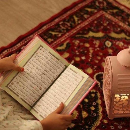 Person reading the Quran on patterned carpet next to a lantern