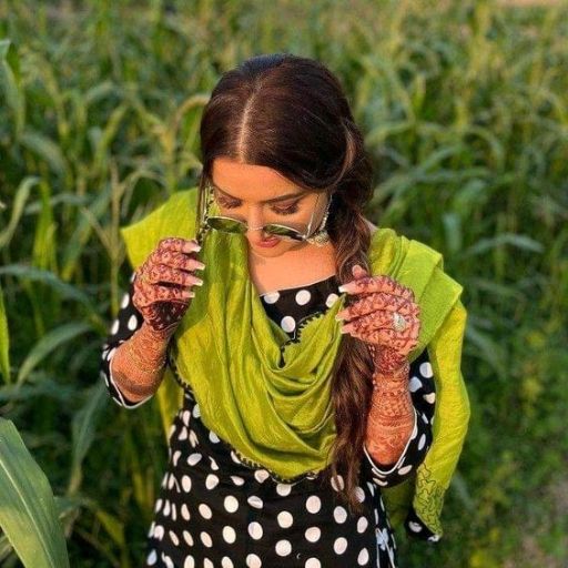 Person with henna on hands wearing a polka dot dress and green scarf, standing in a field