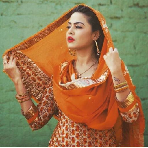 Woman in orange traditional attire with bangles, standing against a green wall