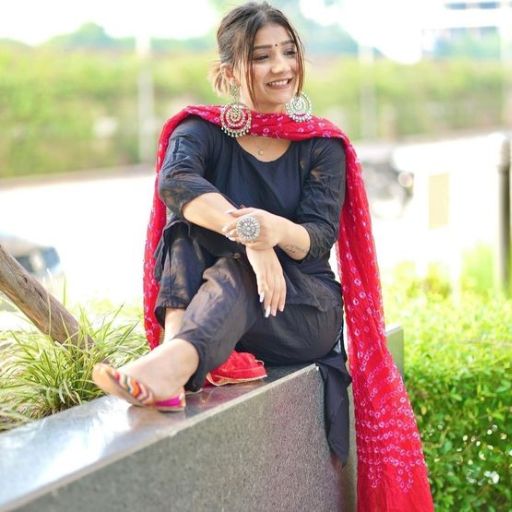 Woman sitting on ledge wearing black attire with red dupatta and sandals